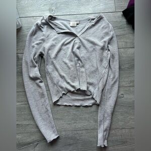 Woman’s gray long sleeve top with ruffle hem on bottom and on ends of sleeves.
